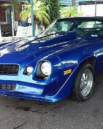 A blue classic Camaro with polished chrome bumpers and clean whitewall tires.
